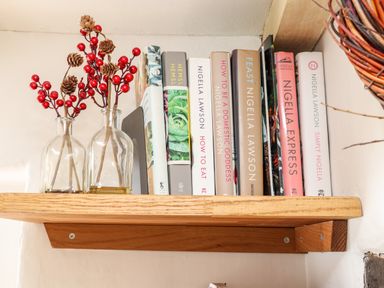 A wooden shelf with cookbooks and two glass bottles with decorative red berries and pine cones at Trelash Cottage in Trelash near Boscastle