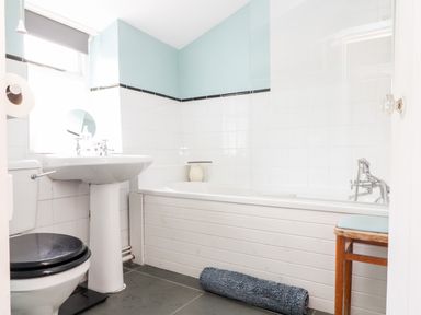 A bathroom with a toilet a pedestal sink a bathtub a small stool and a rolled-up rug at Trelash Cottage in Trelash near Boscastle