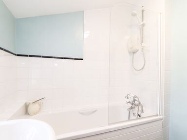 A bathroom with a bathtub shower and white tiled walls at Trelash Cottage Trelash near Boscastle