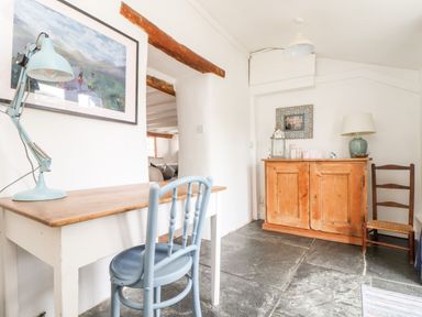 A room with a wooden desk and blue chair a wooden cabinet with a lamp and chair on a stone floor at Trelash Cottage in Trelash near Boscastle