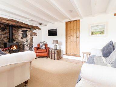A living room with a stone fireplace wood stove a brown leather armchair a white sofa and a wooden door at Trelash Cottage Trelash near Boscastle