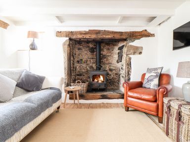 A living room with a wood stove fireplace a leather armchair a sofa with cushions and a lamp at Trelash Cottage Trelash near Boscastle