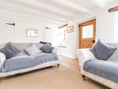 A living room with two sofas and cushions a wooden door and white walls at Trelash Cottage in Trelash near Boscastle