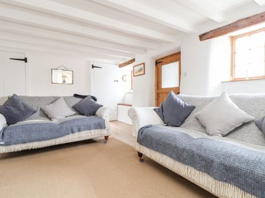 A sitting room with two sofas, cushions, wooden door, and small staircase at Trelash Cottage in Trelash near Boscastle