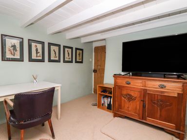 A room with a white table and dark chair a wooden cabinet with a television and framed pictures on the wall at Trelash Cottage Trelash near Boscastle