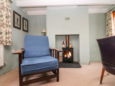 A living room with a blue cushioned wooden armchair and a lit fireplace at Trelash Cottage in Trelash near Boscastle