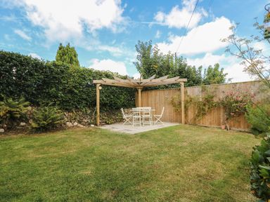 A backyard with wooden pergola and white table with chairs on a stone patio at Trelash Cottage in Trelash near Boscastle