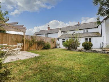 A backyard with a grassy lawn wooden fence patio furniture and shrubs at Trelash Cottage in Trelash near Boscastle