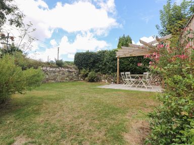 A garden with grass lawn a wooden pergola and outdoor table with chairs at Trelash Cottage Trelash near Boscastle