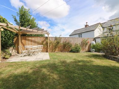 A garden with a wooden pergola and a white outdoor dining set surrounded by grass and a wooden fence at Trelash Cottage in Trelash near Boscastle