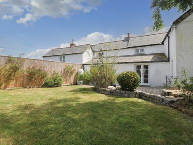A garden with a lawn and plants beside a white house with slate roof at Trelash Cottage in Trelash near Boscastle