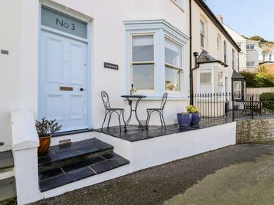 A front porch with a blue door and a small table with two chairs outside Driftwood in Fowey