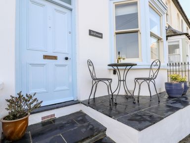 A small outdoor patio with a blue door a round metal table two chairs and plants in pots at Driftwood in Fowey