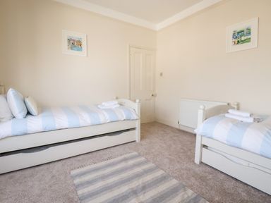 A bedroom with two single beds with blue and white striped bedding a striped rug and framed pictures on the walls at Driftwood in Fowey