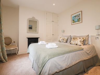 A bedroom with double bed towels on bed chair mirror and built in wardrobe at Driftwood in Fowey