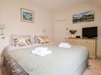 A bedroom with a bed and folded towels two wall paintings a television and a cabinet at Driftwood in Fowey