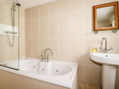 A bathroom with a bathtub shower faucet sink with mirror and soap dispenser at Driftwood in Fowey