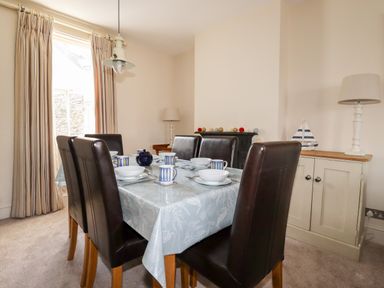 A dining room with a table set with dishes and cups six brown chairs a cabinet with lamps and a model sailboat