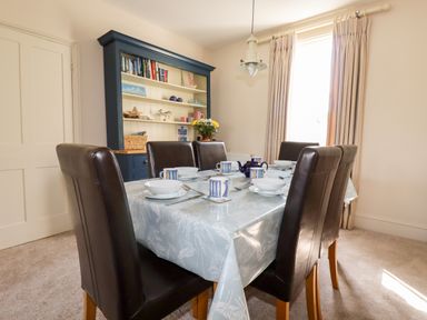 A dining room with a table set for six people and a blue cabinet with shelves at Driftwood in Fowey