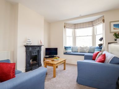 A living room with blue sofas red cushions a wooden coffee table and a window seat at Driftwood in Fowey