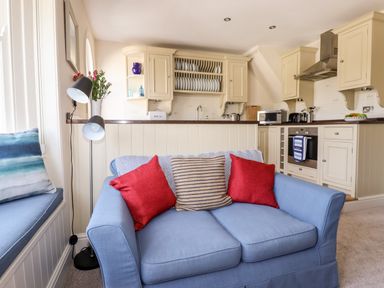A blue sofa with red and striped cushions in front of a kitchen with white cabinets and a dish rack at Driftwood in Fowey