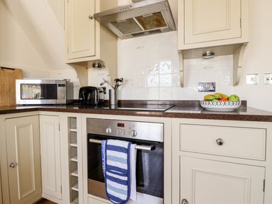 A kitchen counter with a microwave toaster utensil holder oven and a bowl of fruit at Driftwood in Fowey