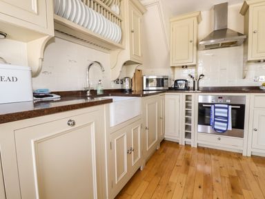 A kitchen with cream cabinets a microwave toaster oven and a sink at Driftwood in Fowey