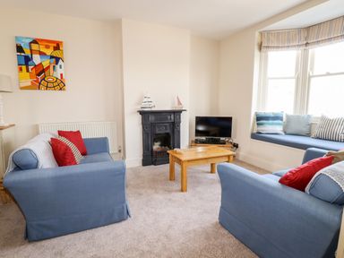 A living room with blue sofas red cushions a wooden coffee table and a TV on a stand at Driftwood in Fowey