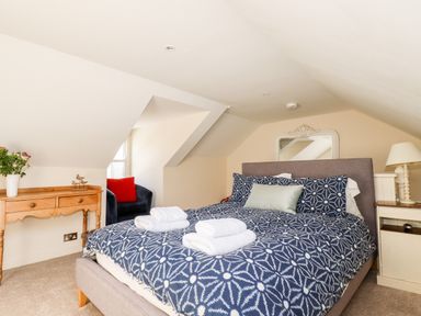 A bedroom with a double bed towels on the bed a wooden side table with flowers and a chair by a window at Driftwood in Fowey