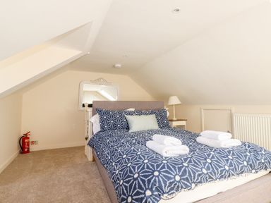 A bedroom with a bed made with patterned blue bedding a bedside table with a lamp and a fire extinguisher in the corner at Driftwood in Fowey