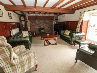 A living room with green leather sofas a plaid armchair a wooden coffee table a brick fireplace and exposed wooden beams at The Granary in Longhirst near Morpeth