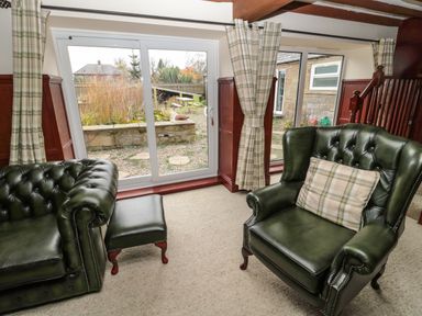 A room with two green leather armchairs a footstool and large windows with plaid curtains at The Granary in Longhirst near Morpeth