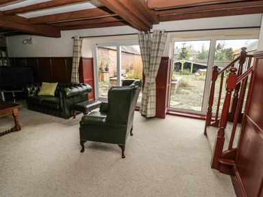 A living room with green leather sofa and chair near sliding glass doors leading to a garden at The Granary in Longhirst near Morpeth