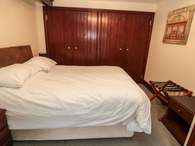 A bedroom with a bed white bedding wooden bedside table luggage rack and wooden closets at The Granary in Longhirst near Morpeth