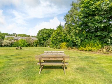 An outdoor grassy area with wooden picnic tables and trees in the background at The Granary in Longhirst near Morpeth