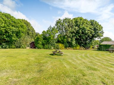 A large grassy garden area with picnic tables surrounded by trees and a small shed at The Granary in Longhirst near Morpeth