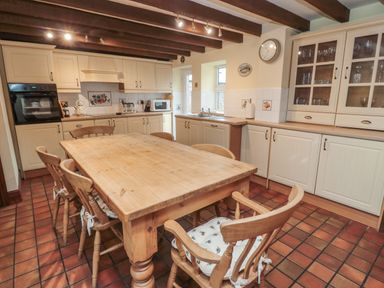 A kitchen with a wooden dining table and six chairs with cushions and cabinetry with appliances at The Granary in Longhirst near Morpeth