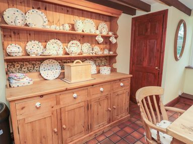 A wooden kitchen dresser with polka dot crockery and a bread box by a wooden door and a chair at The Granary in Longhirst near Morpeth