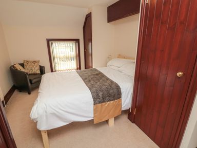 A bedroom with a double bed a black armchair with cushions a small window and wooden doors at The Granary in Longhirst near Morpeth