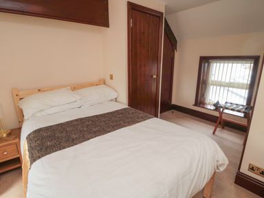 A bedroom with a double bed a bedside table a window with blinds and a wooden door at The Granary in Longhirst near Morpeth