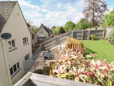 A garden with a lawn, plants, a patio area with a table and chairs, and a fenced house at White Stones in Fulbrook near Burford