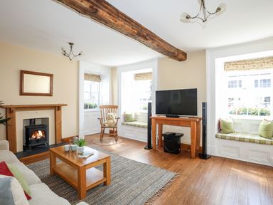 A living room with a wooden beam ceiling a fireplace a rocking chair and two window seats at Above Deck in Beaumaris