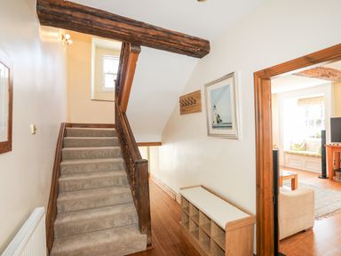A staircase with carpet and wooden banister next to a wooden framed doorway leading to a living room with a window seat at Above Deck in Beaumaris