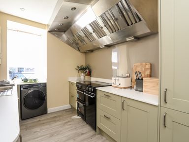 A kitchen with green cabinets a black oven a toaster a knife block a bread box and a washing machine at Above Deck in Beaumaris