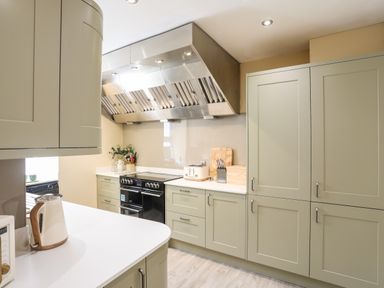 A kitchen with green cabinets white countertops a black stove and stainless steel extractor hood at Above Deck in Beaumaris