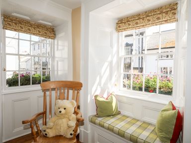 A corner with two windows a wooden rocking chair with a teddy bear and a built-in bench with cushions at Above Deck in Beaumaris