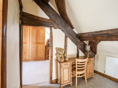 A wooden desk with a chair and a teddy bear under exposed wooden beams in a room next to a doorway showing a wardrobe
