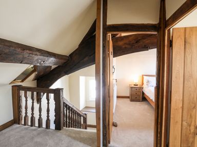 A hallway with wooden beams and carpeted floor leading to a bedroom with a wooden bed and nightstand at Above Deck in Beaumaris