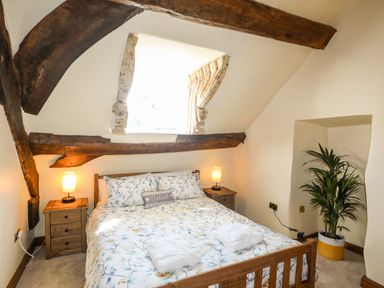 A bedroom with a wooden bed floral bedding two bedside tables with lamps a potted plant and exposed wooden beams at Above Deck in Beaumaris