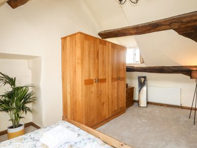 A bedroom with a wooden wardrobe a plant bed with floral bedding a standing mirror and wooden beams at Above Deck in Beaumaris